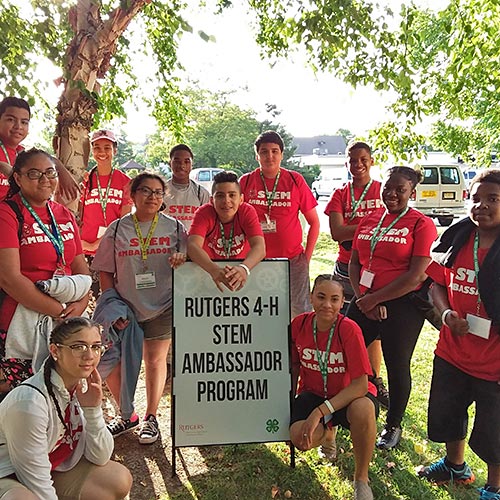 A group of 4-H STEMP Ambassadors standing around a sign that says, 'Rutgers 4-H STEM Ambassador Program'.