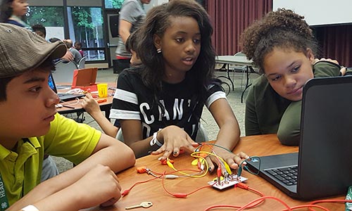 Three children working on electronics connected to a laptop computer.